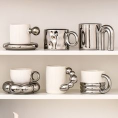 several coffee cups and mugs sitting on top of white shelves with silver metal handles