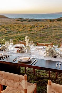 a table set up with place settings and flowers on it in front of the ocean