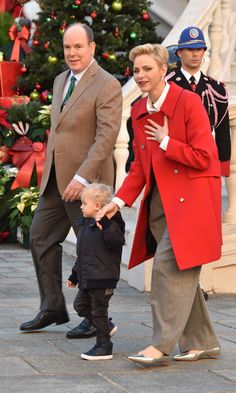 a man and woman holding hands with a small child in front of a christmas tree