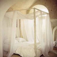 a canopy bed with white sheets and curtains on it's sides, in a bedroom