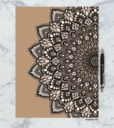 a spiral notebook with an intricate design on the cover and a pen next to it