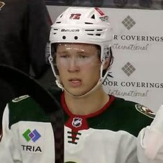 a young man wearing a white and green hockey uniform with his hands in the air