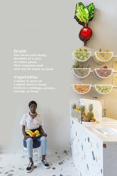 a woman sitting in front of a wall with fruit on it