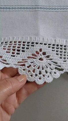 someone is holding the edge of a piece of white fabric with crocheted lace