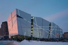 a large building is lit up in the evening with snow on the ground and buildings behind it