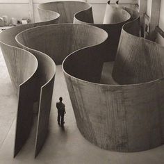 a black and white photo of a person standing in front of an abstract structure with curved sections