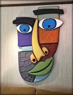 a colorful mask with blue eyes and a banana on it's face is hanging on the wall