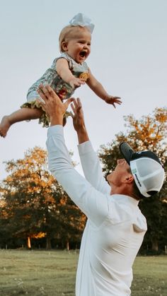 a man holding a baby up in the air while wearing a baseball cap and white shirt