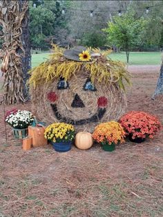 a scarecrow made out of hay surrounded by flowers and pumpkins in front of a tree