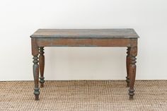 an old wooden table sitting on top of a carpeted floor next to a white wall