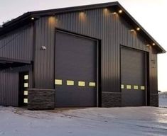 a large black building with two doors and lights on it's sides in the snow