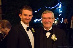 two men in tuxedos standing next to each other at a formal event with blue lights behind them