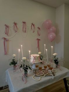 a table topped with a cake covered in frosting and lots of pink balloons hanging from the ceiling