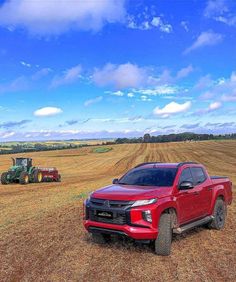 a red truck parked in the middle of a field next to a tractor and plow