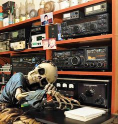 a skeleton sitting on top of a table in front of radio and other electronic equipment