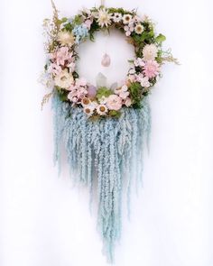 a wreath with flowers and feathers hanging on the wall next to a white wall background