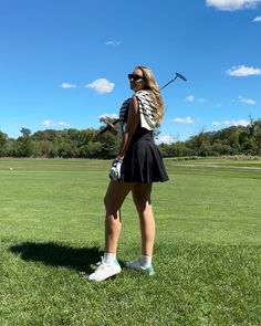 a woman standing on top of a lush green field holding a golf ball and club