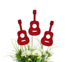 three red guitars are sitting on top of some flowers in a vase with daisies