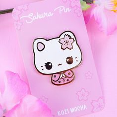 a hello kitty brooch sitting on top of a pink card next to some flowers