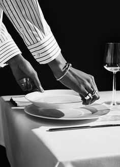 a person is setting a plate on a table with wine glass and utensils