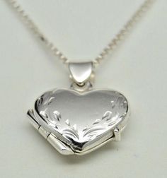 "Photos are precious and here's a lovely way to keep those memories close. Our beautifully worked genuine 925 sterling silver heart picture locket has a hand engraved leaf border along the heart shape itself - so each is a unique work of art. There's also a secure compartment inside to hold two special photos. Our picture locket in genuine sterling silver is small, measuring approx. 5/8\" wide by 3/4\" long - it works as a pendant or as a charm on a bracelet. A lovely piece of jewelry for a youn Heart-shaped Sterling Silver Locket Necklace For Weddings, Sterling Silver Heart Locket Necklace For Wedding, Engraved Sterling Silver Locket Necklace, Sterling Silver White Gold Heart Charm Locket Necklace, White Gold Locket Necklace Stamped 925 For Gift, White Gold Sterling Silver Locket Necklace With Heart Charm, Heart Shaped Sterling Silver Locket Necklace For Anniversary, Sterling Silver Heart Locket Necklace For Anniversary, Silver Heart-shaped Locket Necklace For Anniversary