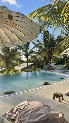 an open umbrella next to a swimming pool with lounge chairs and trees in the background