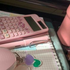 a pink calculator sitting on top of a desk next to a cup and pen