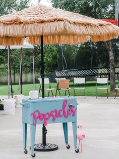 a pink flamingo standing in front of a blue cooler with the word popsicle written on it