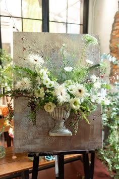 an easel with flowers and greenery in it