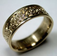 a gold wedding ring with an intricate design on the outside and inside, sitting on a white surface