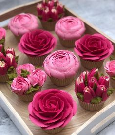 cupcakes decorated with pink frosting and flowers on a wooden tray, ready to be eaten