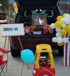 the back of a car with balloons and movies on it's trunk, in front of a drive - in sign