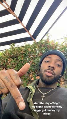 a man pointing at the camera while wearing a black shirt and beanie with writing on it