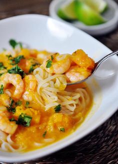 a white bowl filled with pasta and shrimp on top of a wooden table next to limes