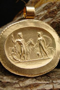 a gold pendant with an image of two men and a woman in ancient greek dress