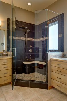 a bathroom with a walk in shower next to a sink and drawers under a window