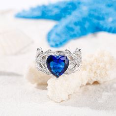 a blue heart shaped ring sitting on top of white sand