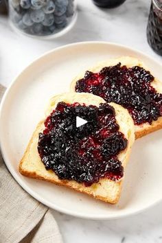 two pieces of bread with jam on them sit on a plate next to blueberries