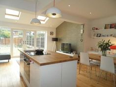 an open kitchen and living room area with wood flooring, white walls and ceiling lights