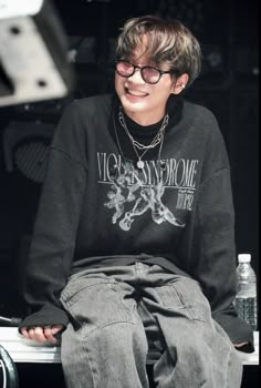 a young man sitting on top of a white bench wearing glasses and a black shirt