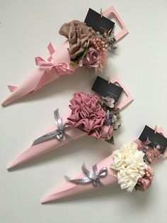 three pink and white flowers are placed in the shape of cones with tags on them