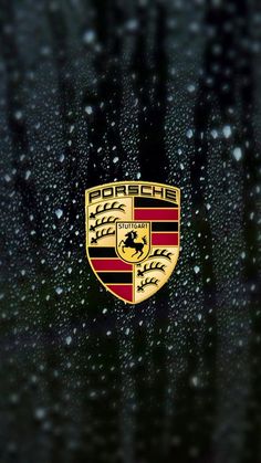 the front end of a porsche logo on a wet window with drops of water around it