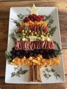 a christmas tree made out of different types of food on a white platter with olives, berries and pine cones