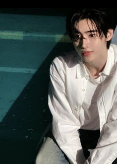 a young man sitting on the ground next to a swimming pool with his hands in his pockets