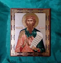 an icon of jesus holding a paper with the words, in gold and green on a blue background