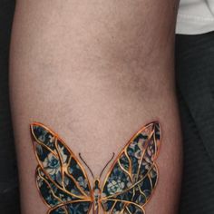 a close up of a butterfly tattoo on a person's leg with gold and blue flowers