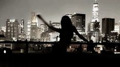 a woman standing in front of a cityscape at night with her arms outstretched