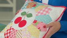 a woman is holding a pillow made with patchwork and cherries on the front