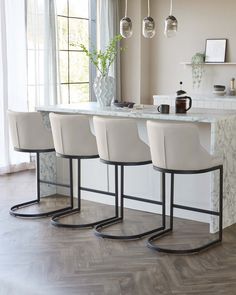 three white chairs sitting at a bar in a room with wood flooring and windows