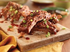 two pieces of meat on a cutting board with sauce and scallions around them